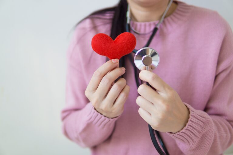Unrecognizable female with stethoscope on neck standing with red heart in hand in daylight